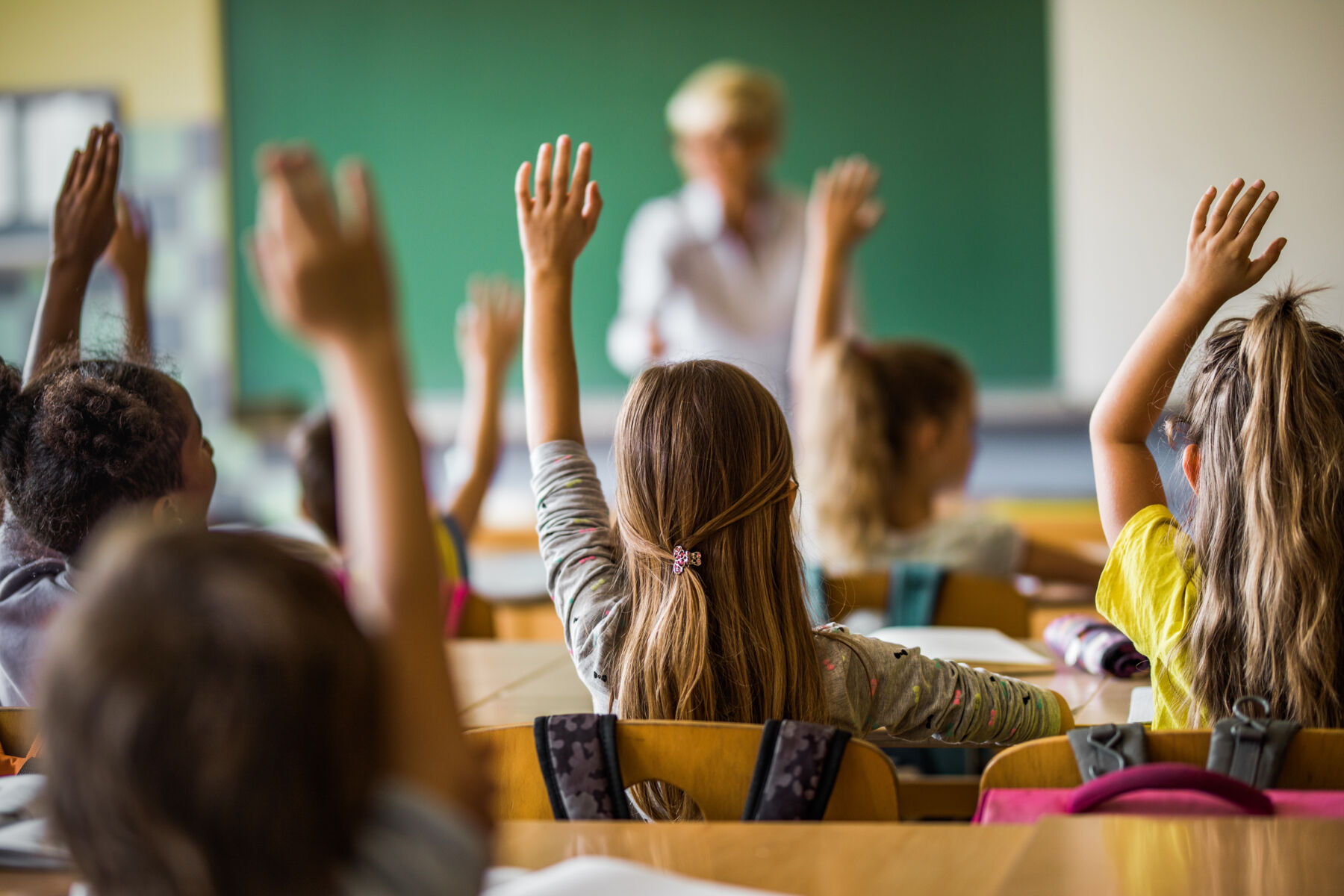 Elementary students raising hands in a classroom