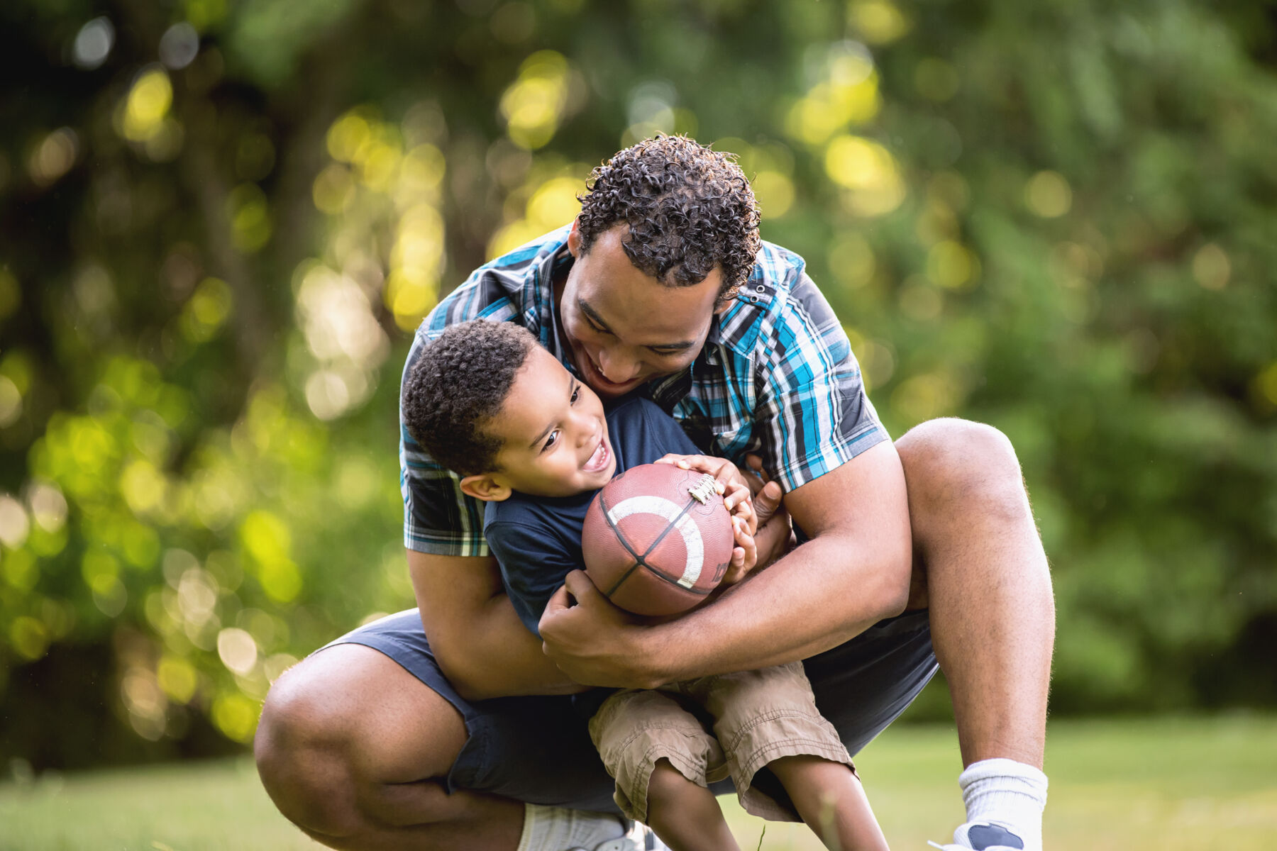 Father and son playing together with a football outside in the sun