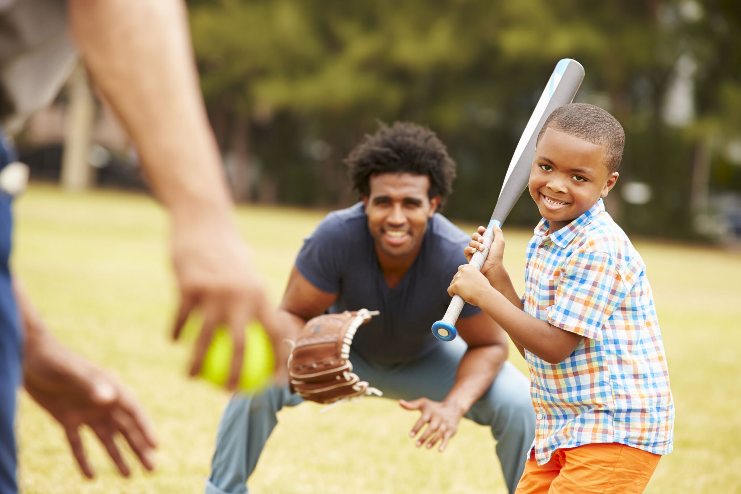 Family playing softball outside in a park.