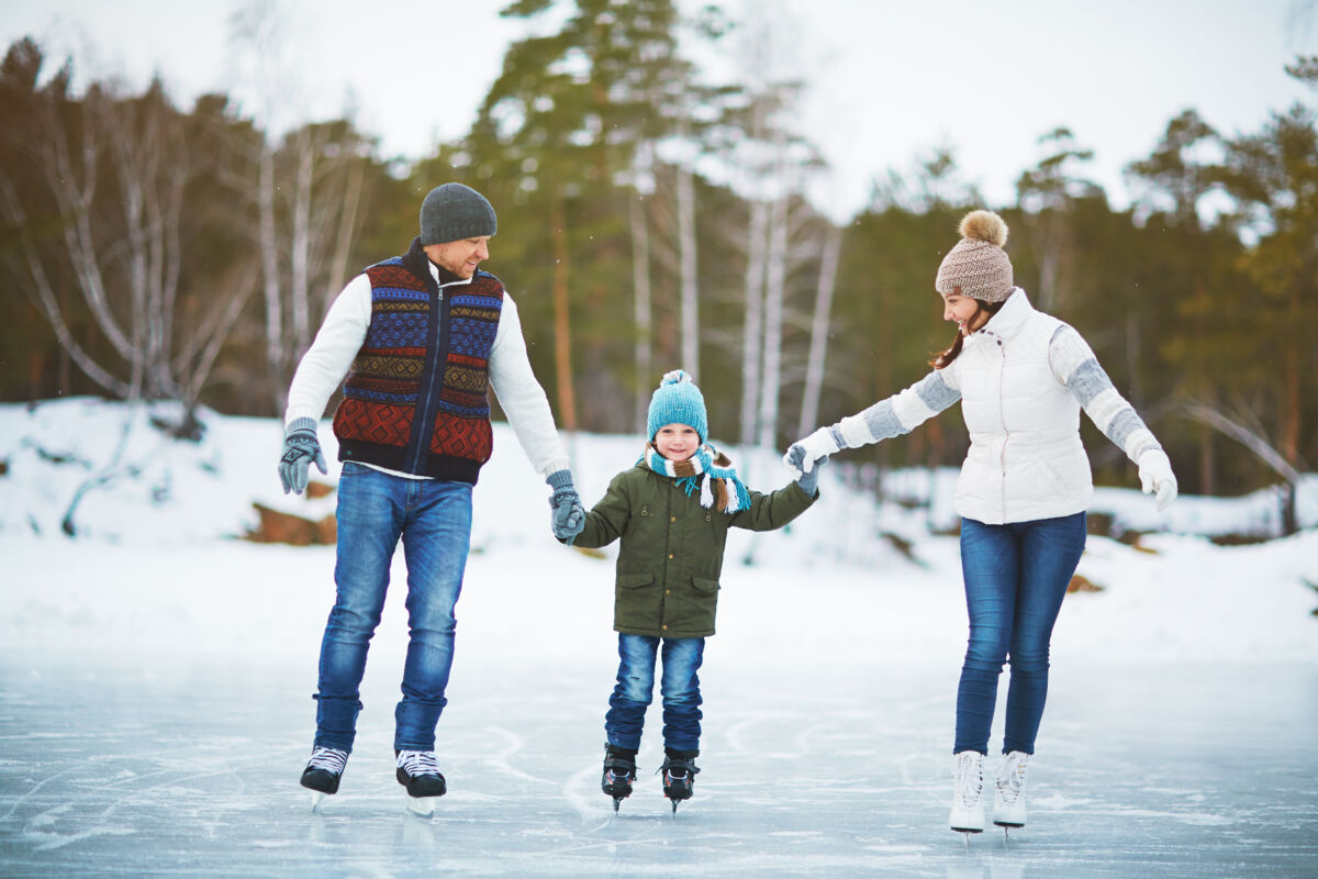 A family, father, mother, and child, ice skating on a lake outside in the winter