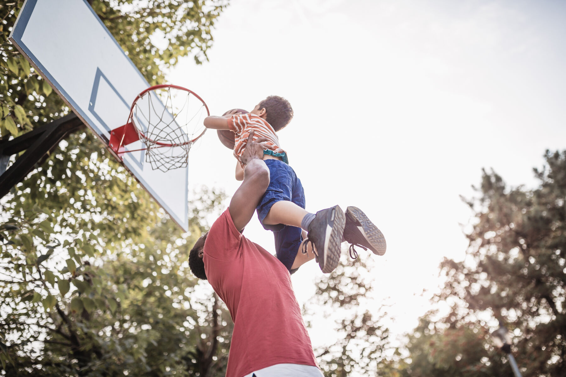 A father helps his son rise to the basketball hoop for a dunk.