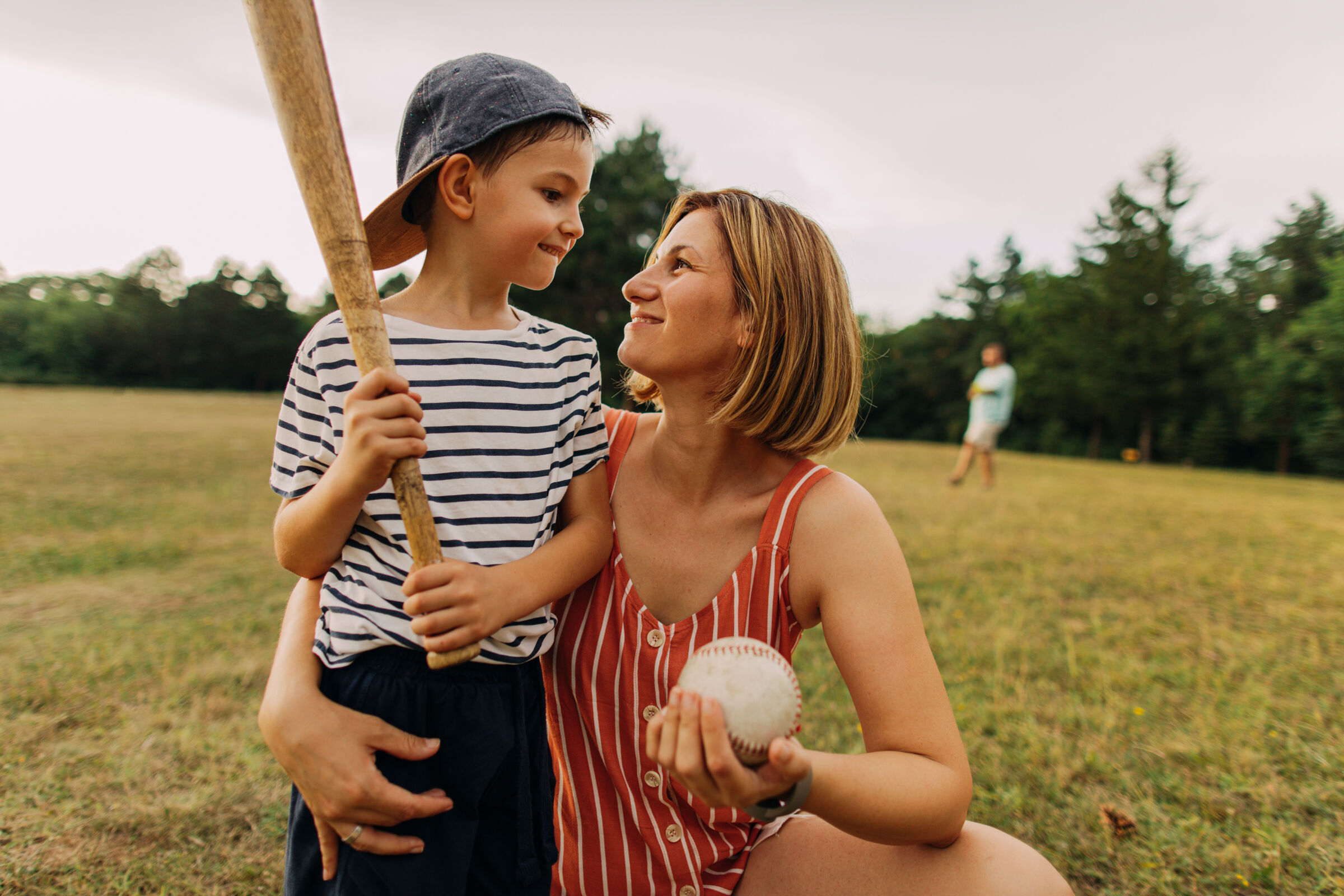 A mother and son enjoy the day outside playing baseball with their family.