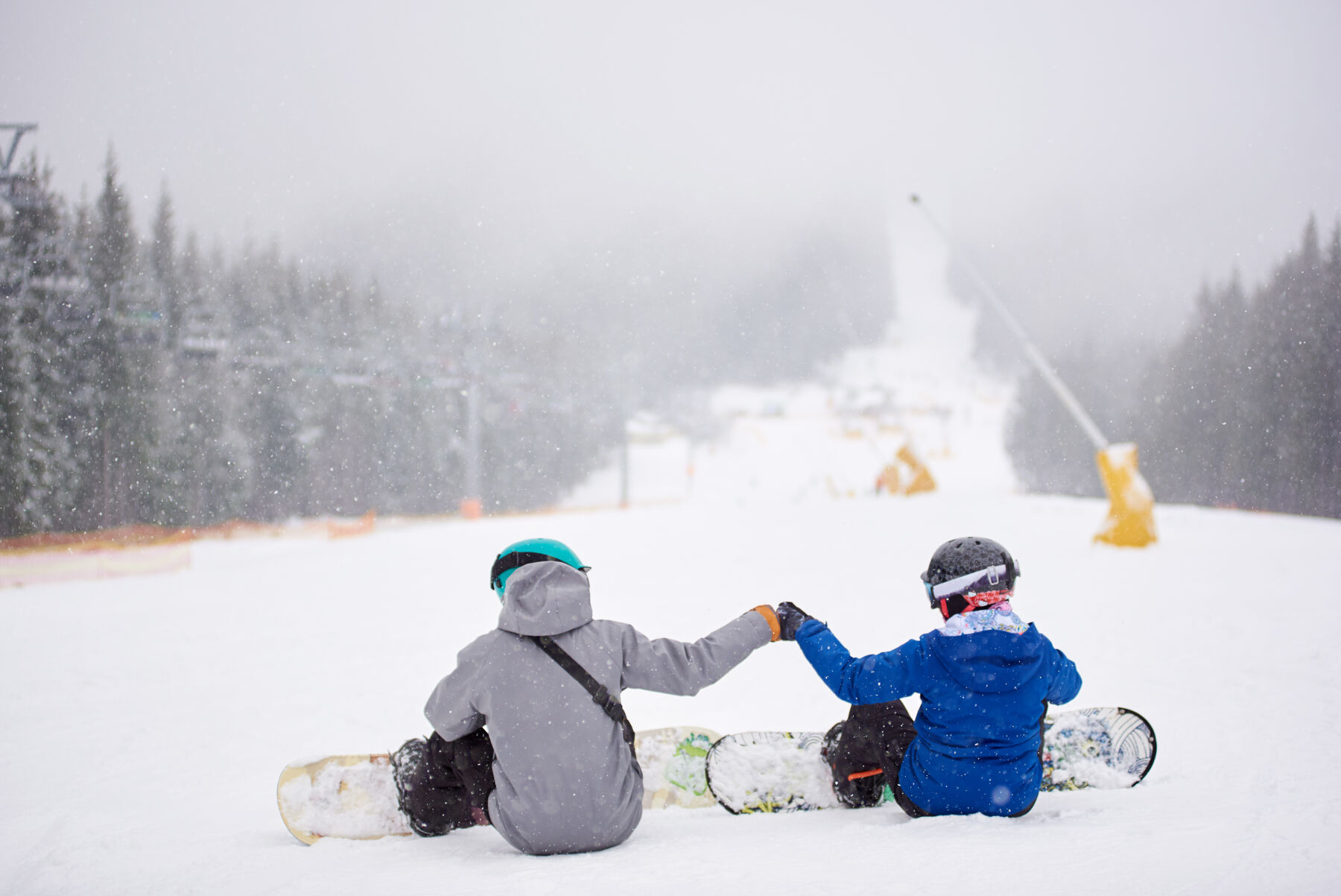 Two friends sit down and bump fists before they snowboard down the mountain.