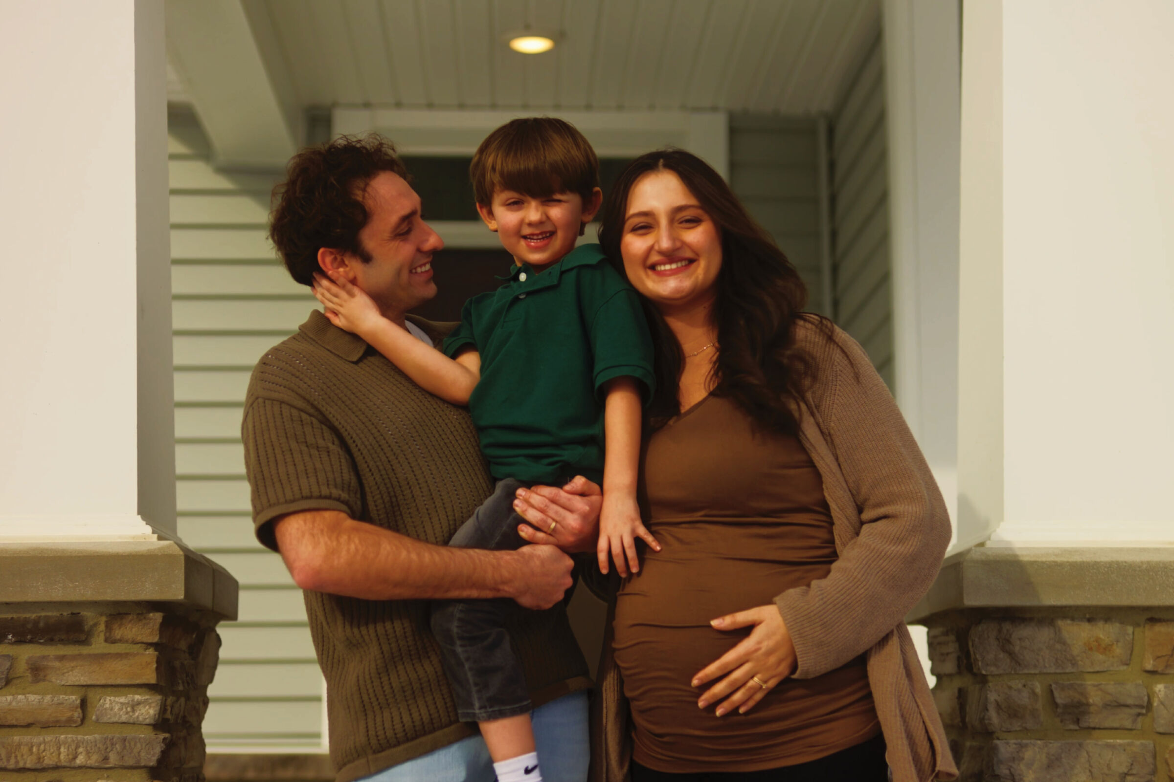 Young family of 3 standing in front of their home